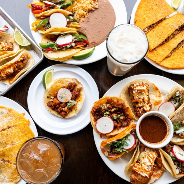 Overhead view of various Casa De Avila Tacos dishes, including tacos, quesadillas, rice, beans, and drinks.
