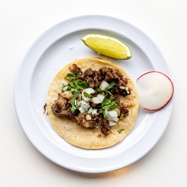 A Casa De Avila Tacos carne asada taco with cilantro and onions, a lime wedge, and radish slice.