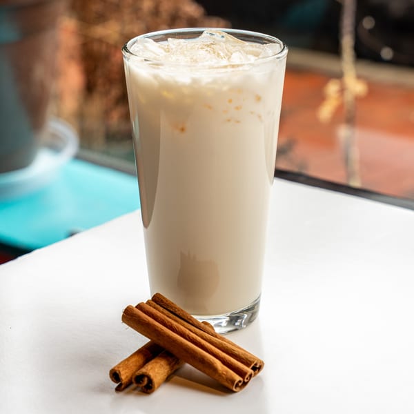 Horchata in a tall glass with ice and cinnamon sticks on a white table.