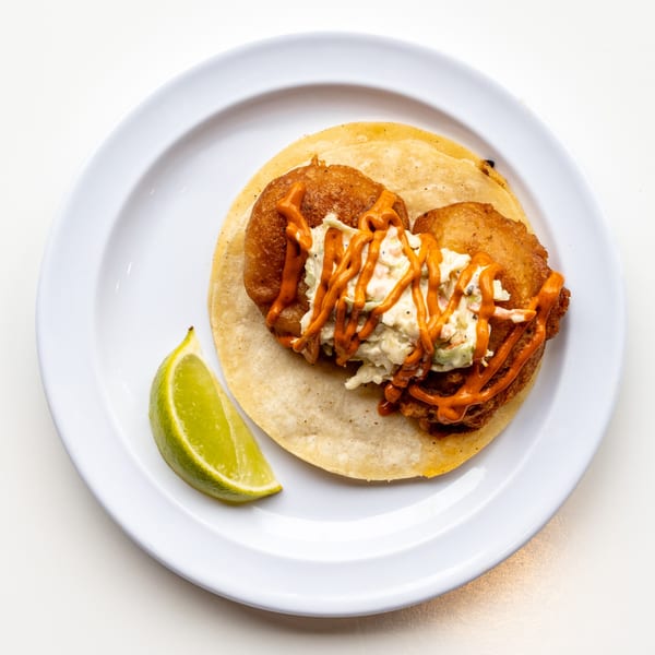 A Casa De Avila Tacos fish taco with slaw and orange sauce, served with a lime wedge.