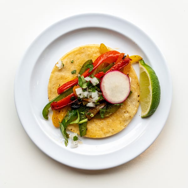 A colorful Casa De Avila Tacos fajita taco with peppers, onions, radish, and lime on a white plate.