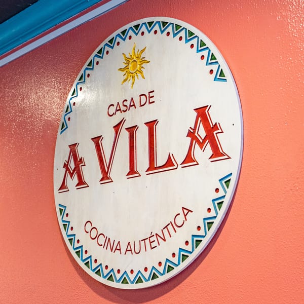Casa De Avila Tacos sign, a white circular sign with red lettering and a sun icon.