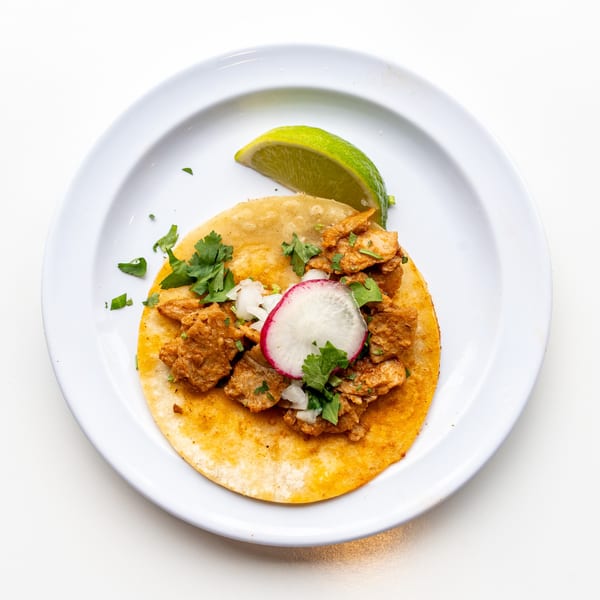 A single Casa De Avila Tacos al pastor taco with radish, onion, cilantro, and a lime wedge.