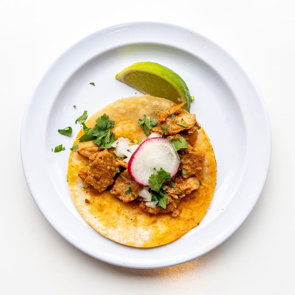 A single Casa De Avila Tacos al pastor taco with radish, onion, cilantro, and a lime wedge.