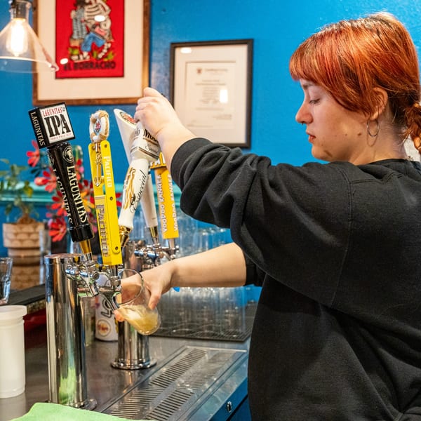 A bartender with red hair pours a beer from a tap at Casa De Avila Tacos.
